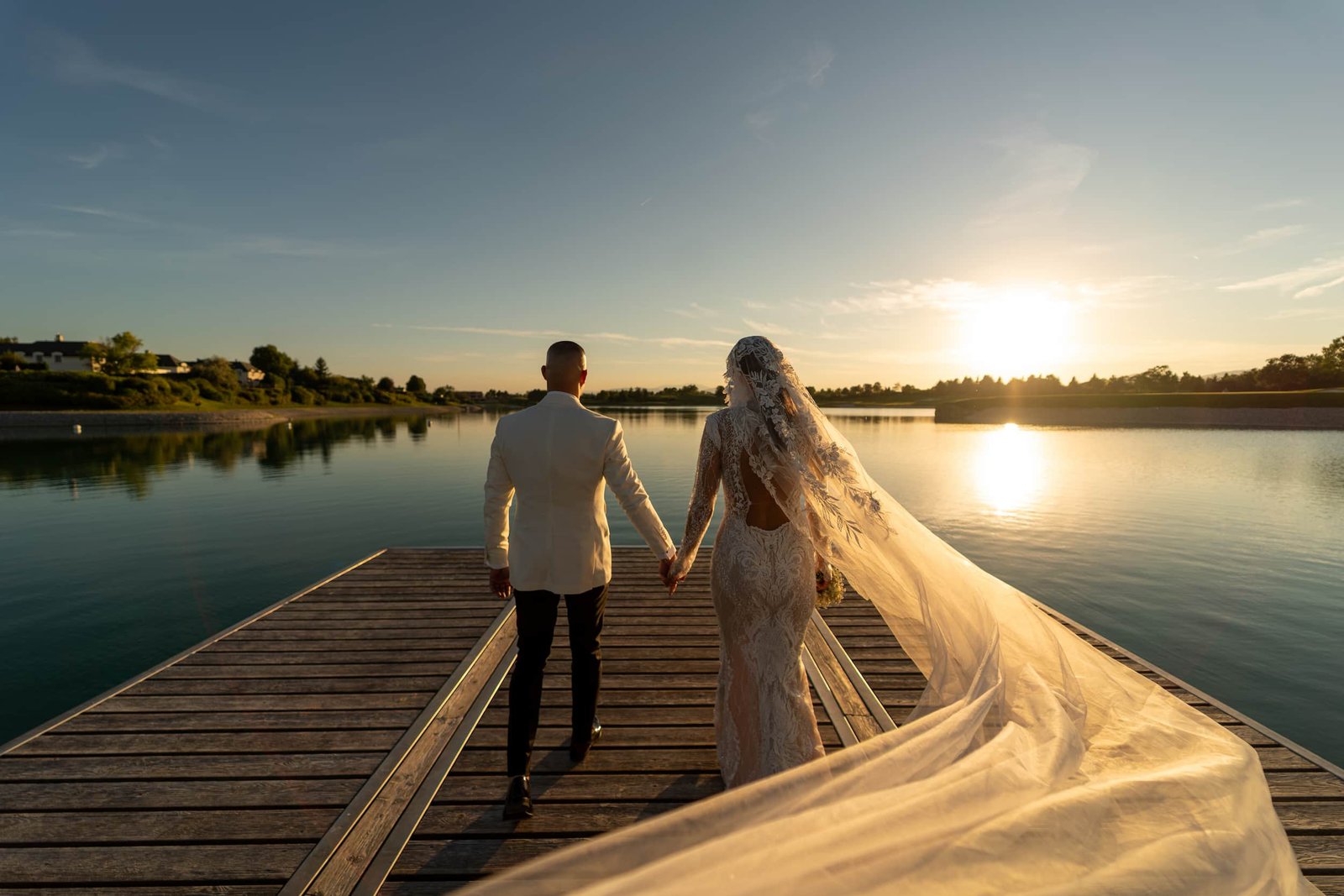 Couple de mariés main dans la main sur un ponton au coucher du soleil